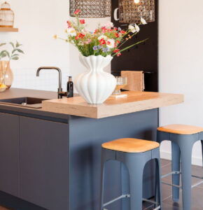 Grijze moderne keuken met verhoogd eiken houten barblad en 2 barkrukken met houten zitting