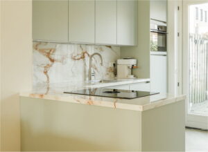 Marmerlook keukenblad en achterwand wit met bruine aders Evora Ceramics Spectacle Lux in licht groene moderne keuken met schier-kookeiland - Binnenkijker uit Rosmalen bij trotse klant van I-KOOK
