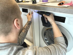 Droger en wasmachine inbouwen stappenplan - vastschroeven van het onderkast frontraam aan het zijwand afdekpaneel Droger en wasmachine inbouwen - vastschroeven van de onderkast frontraam aan het zijwand afdekpaneel