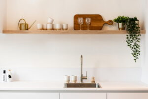 Mat witte keuken greeploos met wandplank voor keukenaccessoires als zand aardetinten kopjes, plantjes en een houten borrelplank